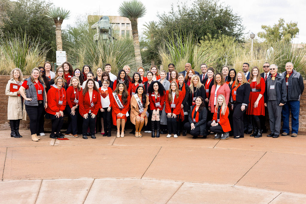 Group of people, mostly wearing red gather in front of arizona state capitol