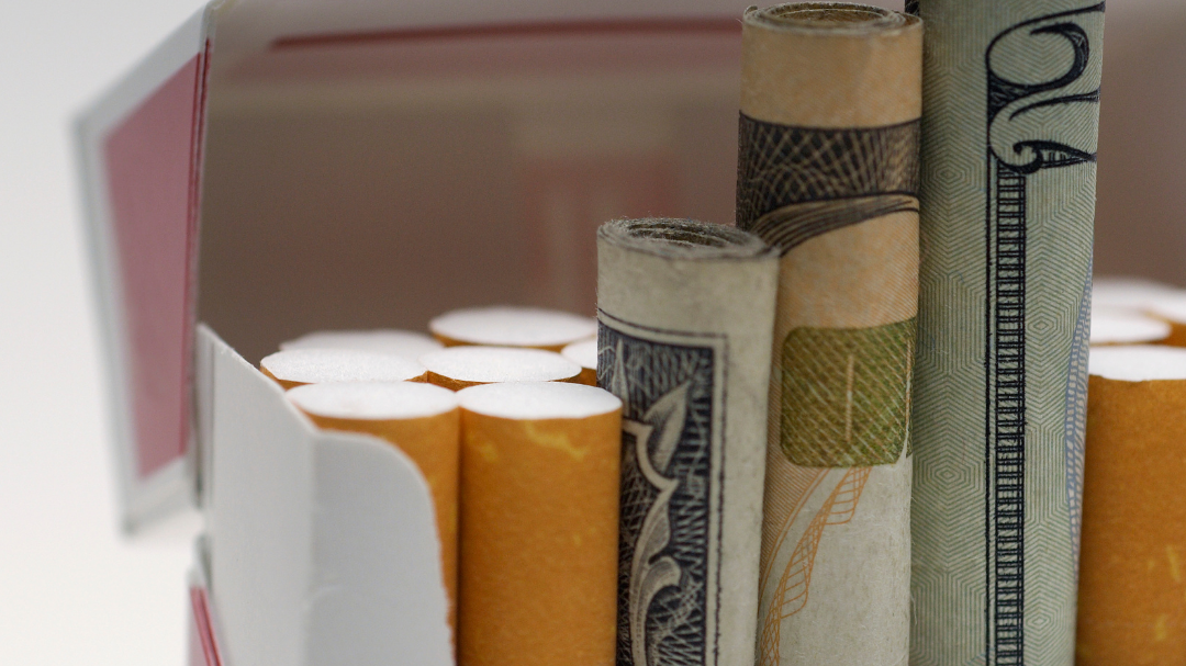 A pack of cigarettes with rolled up dollar bills next to the cigarettes.