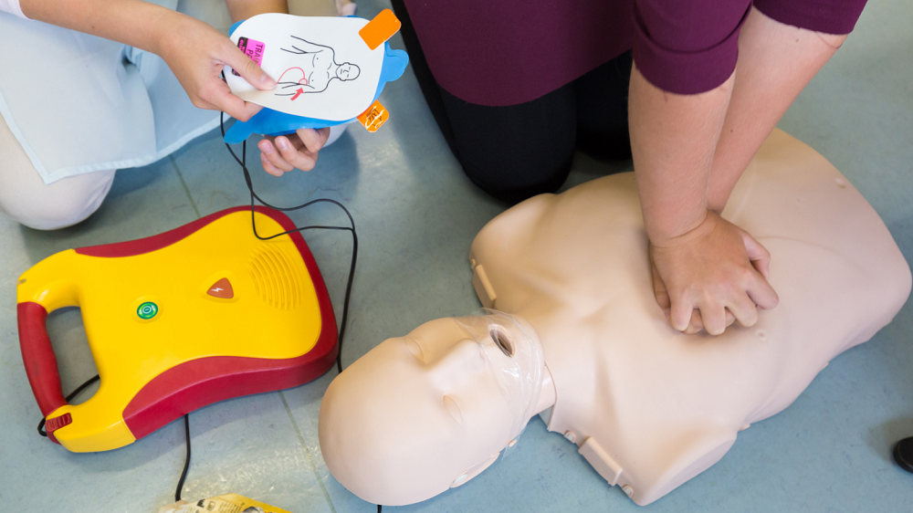 Man practices CPR with an AED nearby.