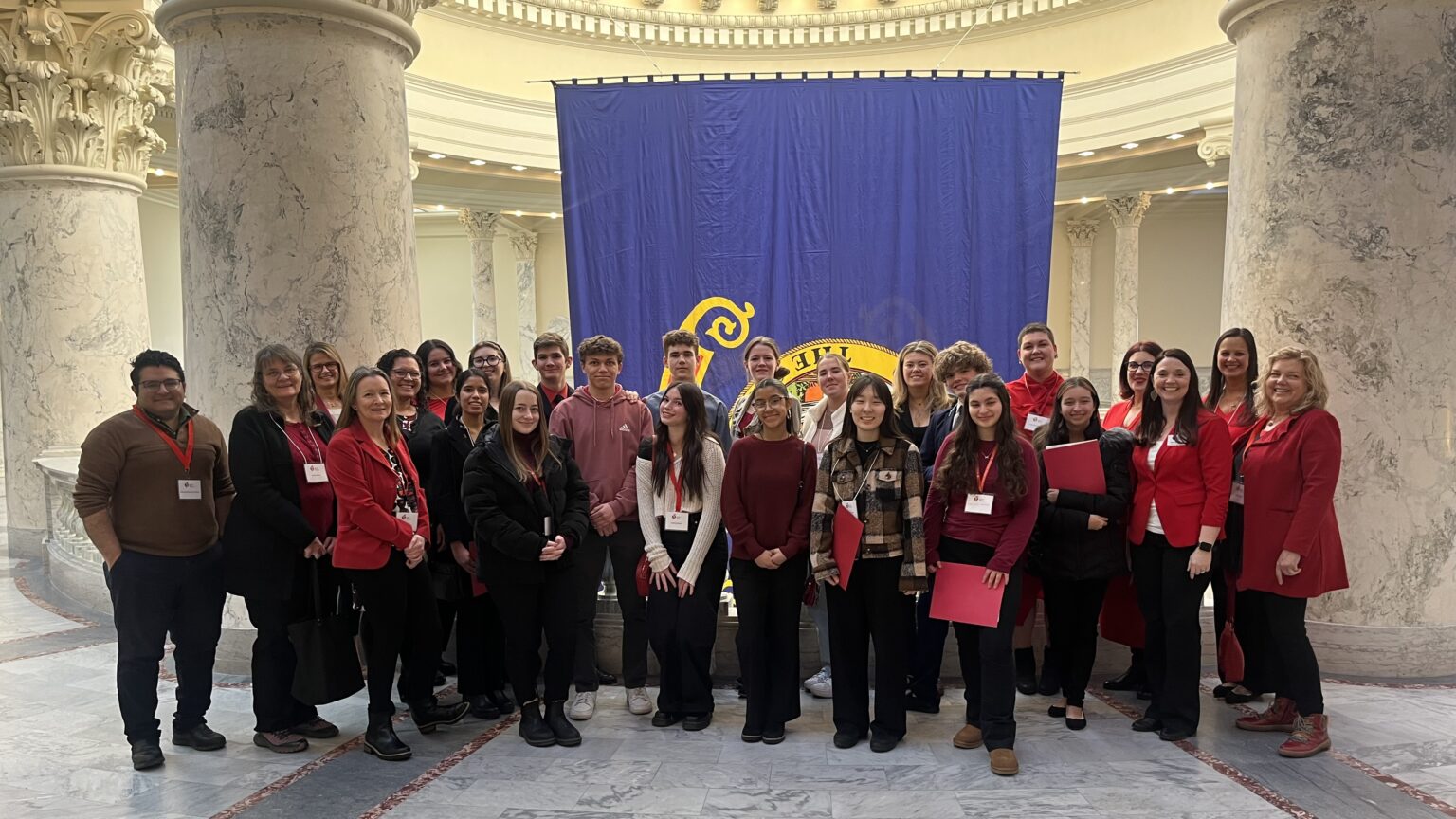 A group of people standing inside the Idaho Capitol building with the state flag behind them.
