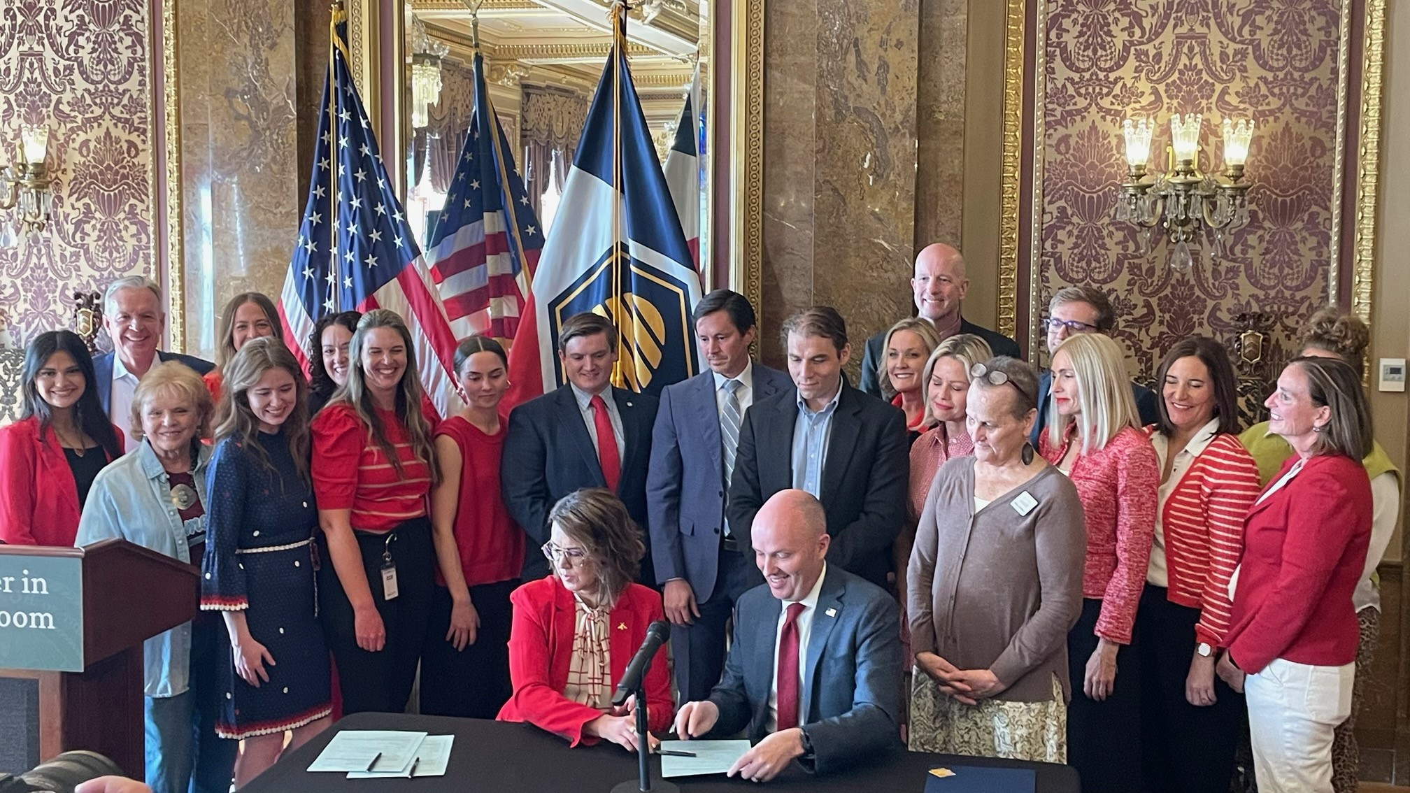 A group of people surrounding the Governor at a desk. They are inside.