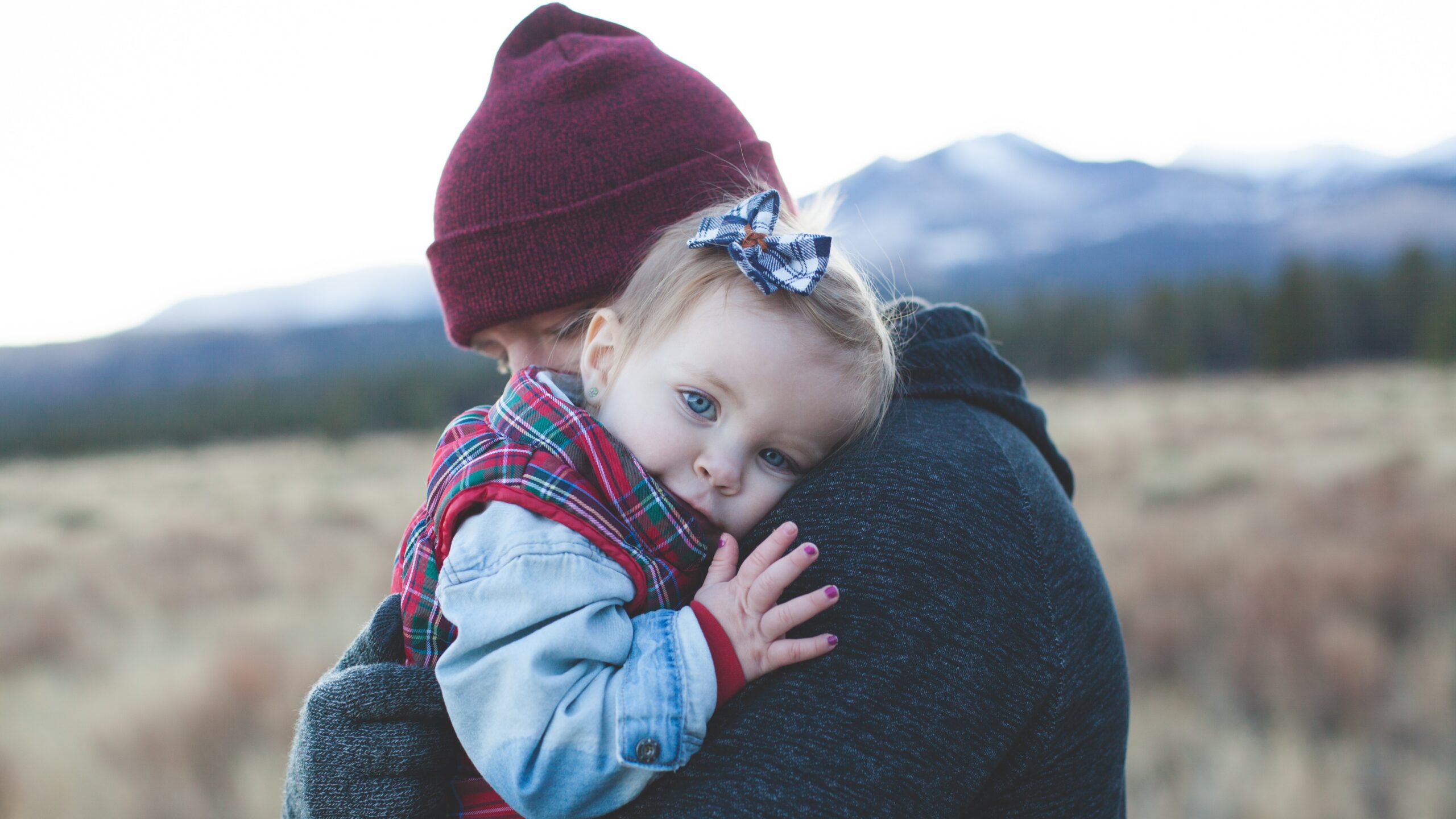 An adult holding a toddler outside wearing fall weather clothes.