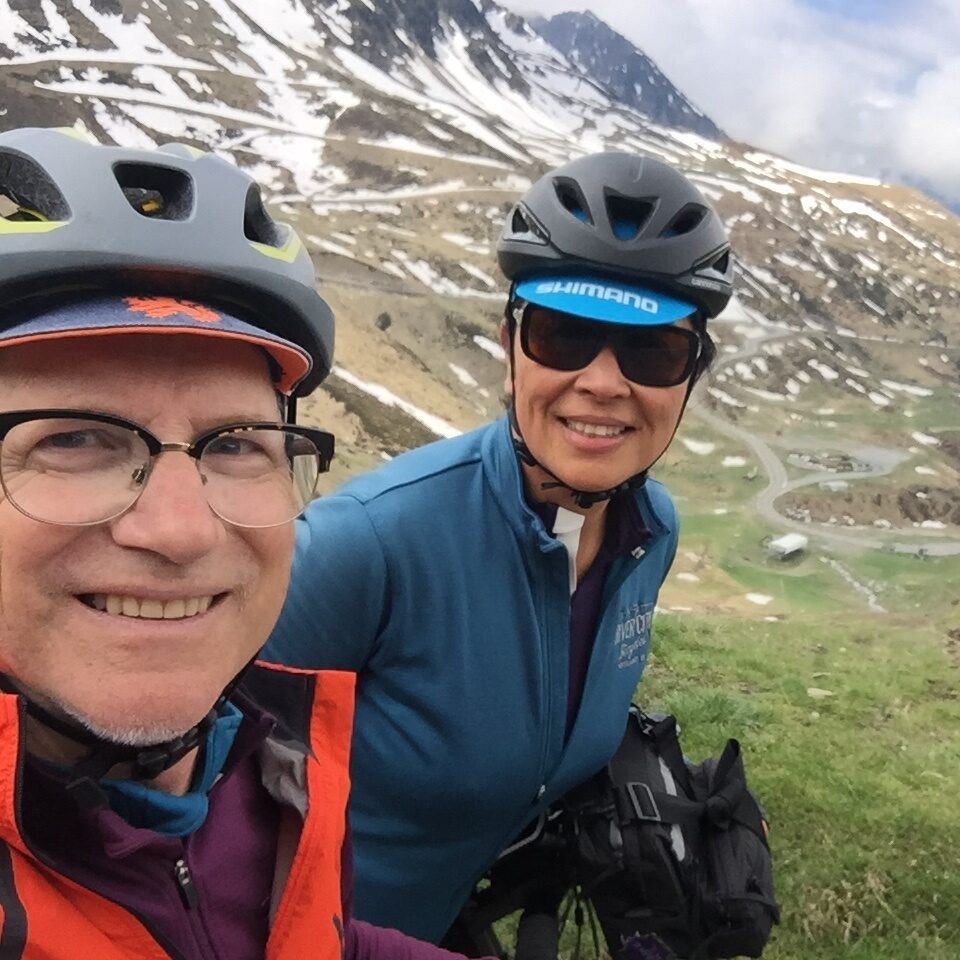 A man and a woman on their bikes in the mountains wearing helmets.